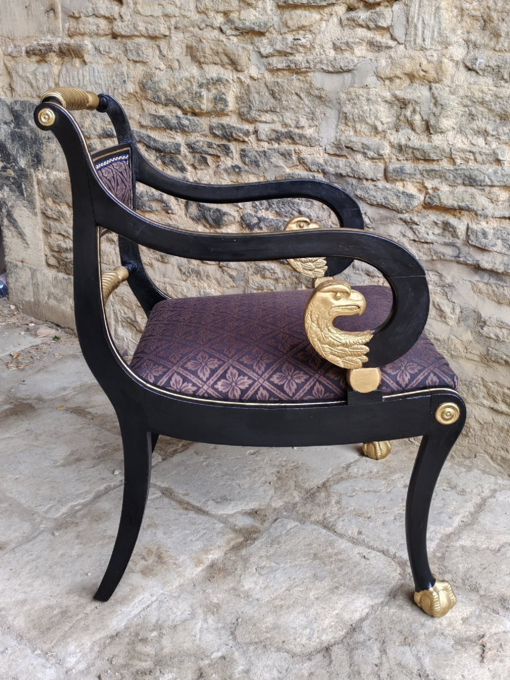 An ebonised and parcel-gilt Regency armchair featuring carved eagle head arm terminals, reeded scroll bars, patterned purple fabric upholstery, and gold paw feet. View VI