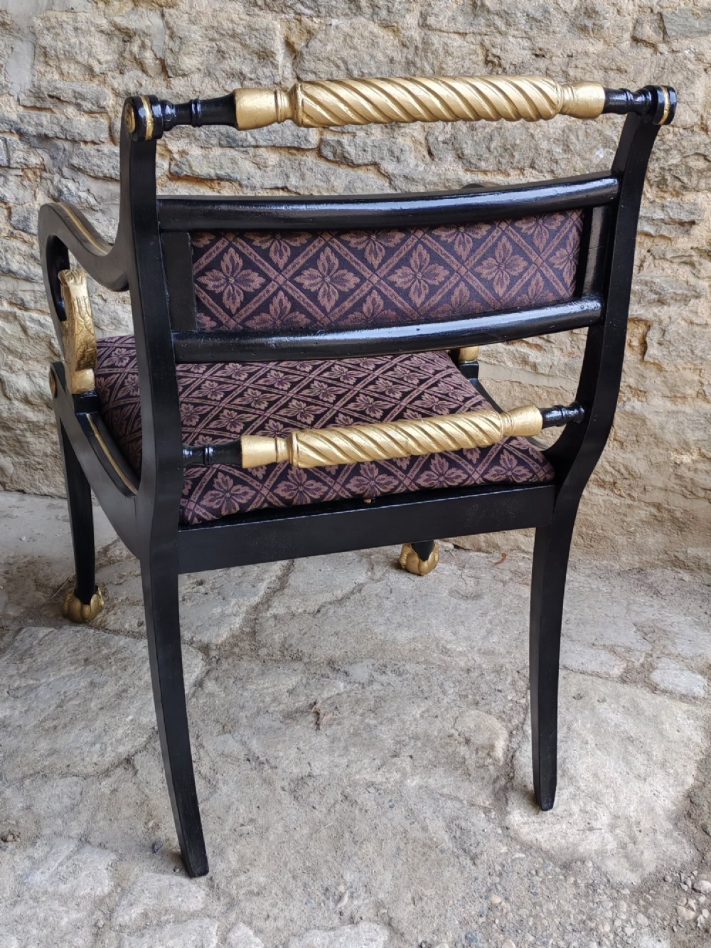 An ebonised and parcel-gilt Regency armchair featuring carved eagle head arm terminals, reeded scroll bars, patterned purple fabric upholstery, and gold paw feet. View X
