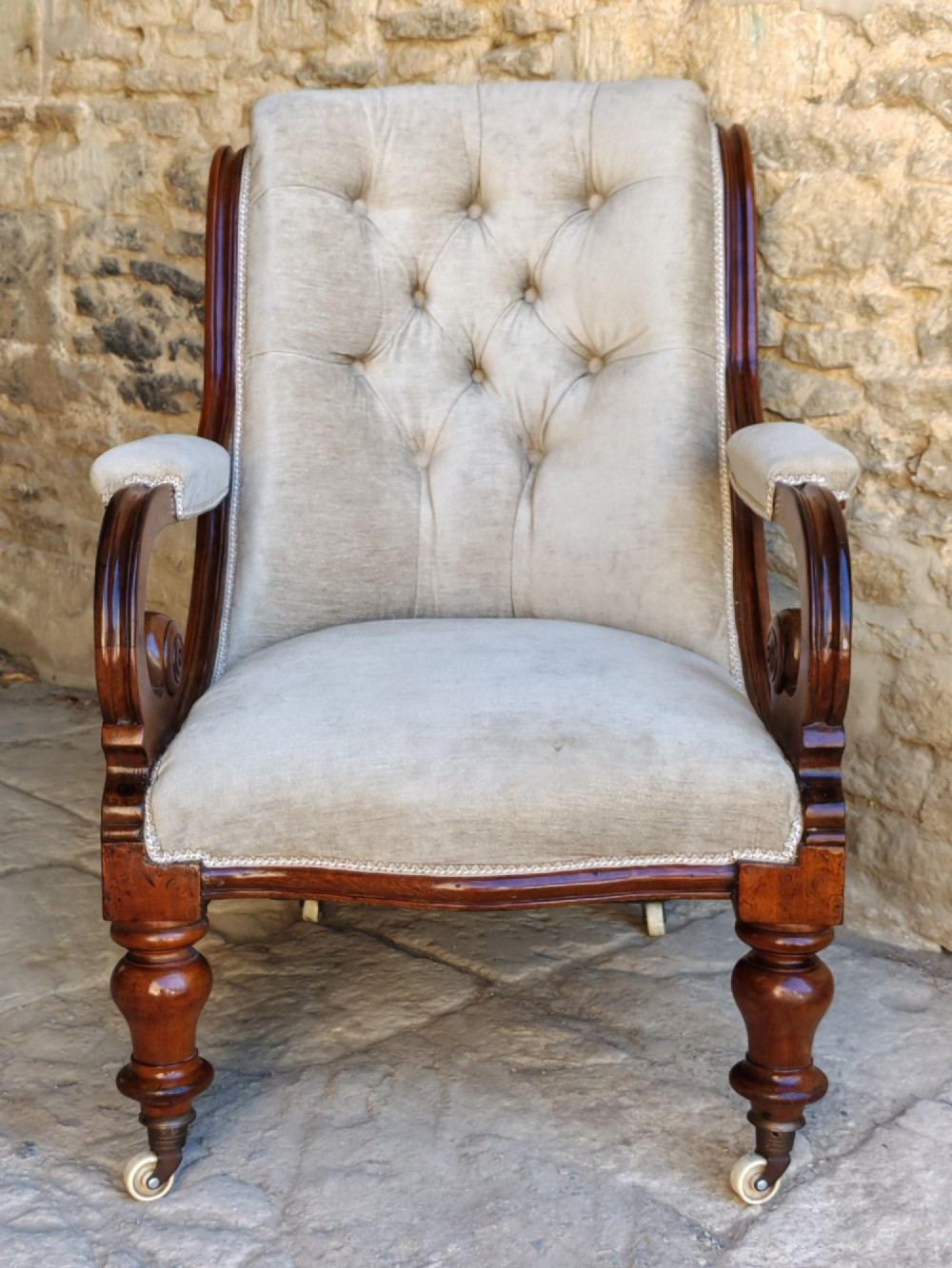 Mid-Victorian walnut armchair featuring light grey button-back upholstery, carved scroll armrests, and turned legs with ceramic casters. View II