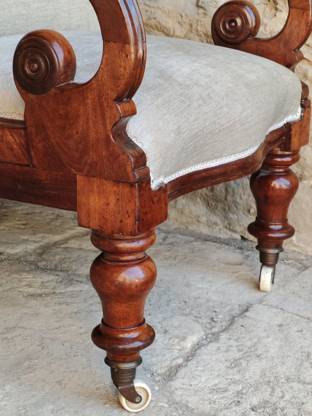Mid-Victorian walnut armchair featuring light grey button-back upholstery, carved scroll armrests, and turned legs with ceramic casters. View VII