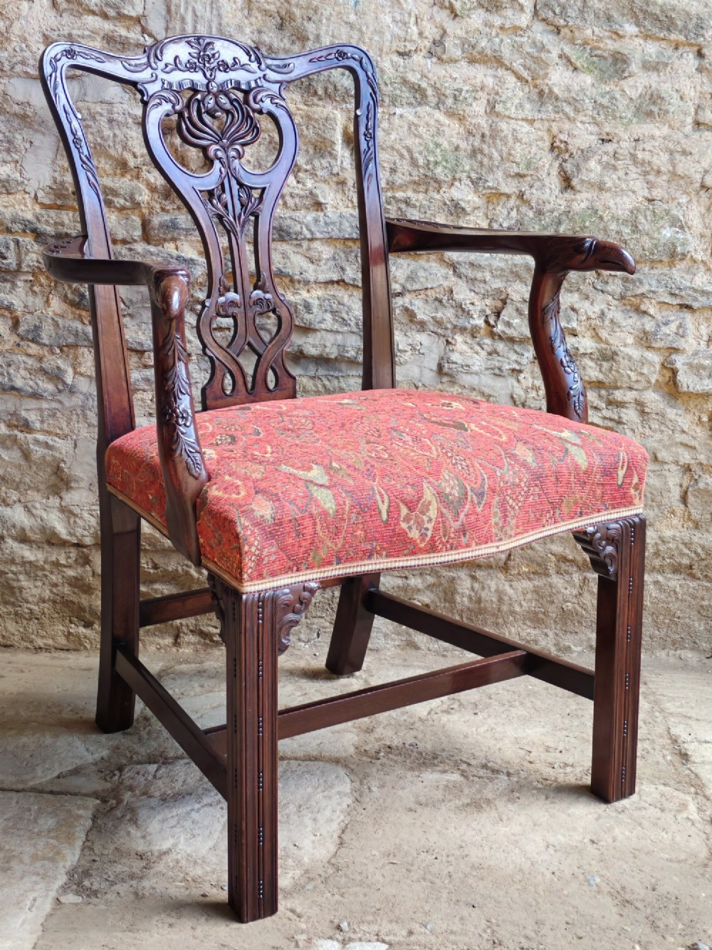 A dark mahogany Chippendale revival carver armchair with an intricately carved splat back and red patterned fabric seat cushion.
