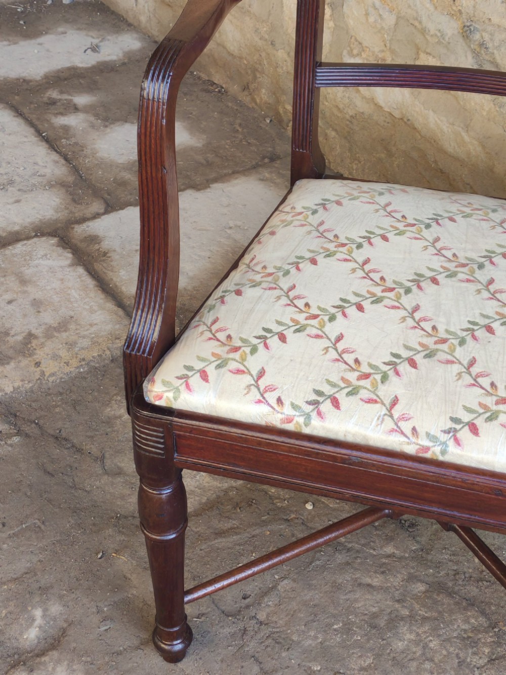 A George III mahogany carver armchair featuring reeded armrests, a carved mid-rail, turned front legs, an X-frame stretcher, and a cream pattern fabric seat. View VI