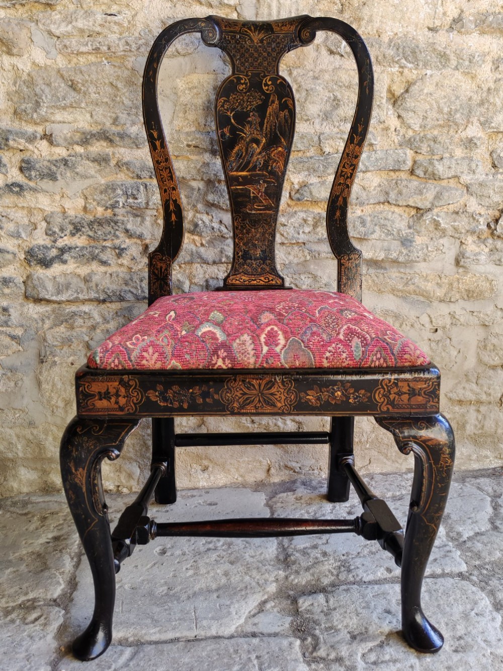 An early 18th-century Queen Anne side chair featuring black japanned lacquer with detailed gold Chinoiserie decorations, a vase splat back, cabriole legs, and a patterned red upholstery seat.