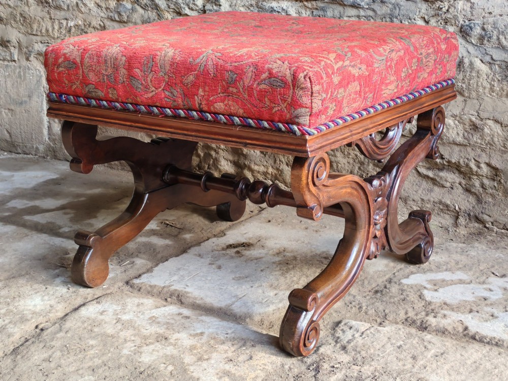 A mid-19th century mahogany X-frame stool featuring carved scroll legs, a central flower motif, and a red patterned upholstered seat with braided trim. View IV
