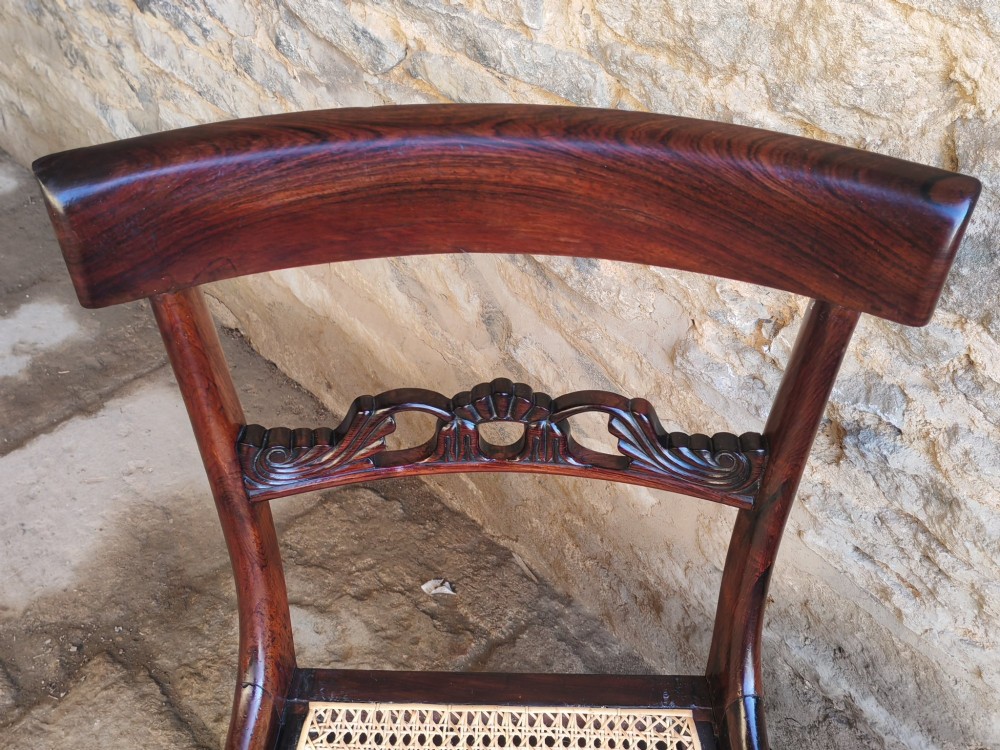 A pair of early 19th-century rosewood dining chairs featuring carved cresting rails, woven cane seats, and turned fluted front legs. View VI