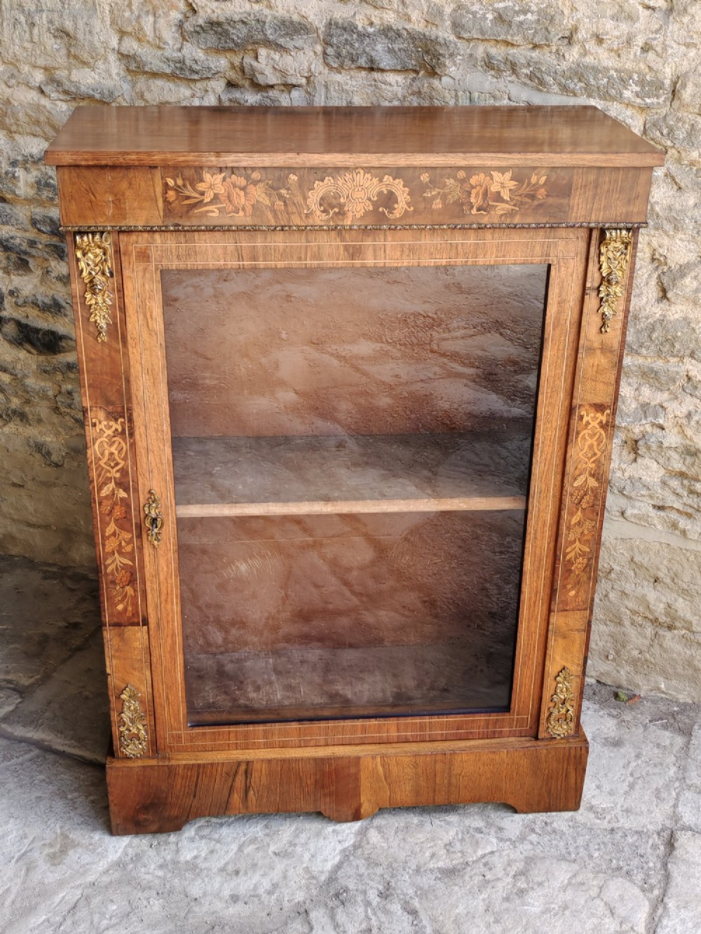 A Victorian walnut pier cabinet featuring floral marquetry inlay, gilt-bronze mounts, and a single glazed glass door opening to two interior shelves.