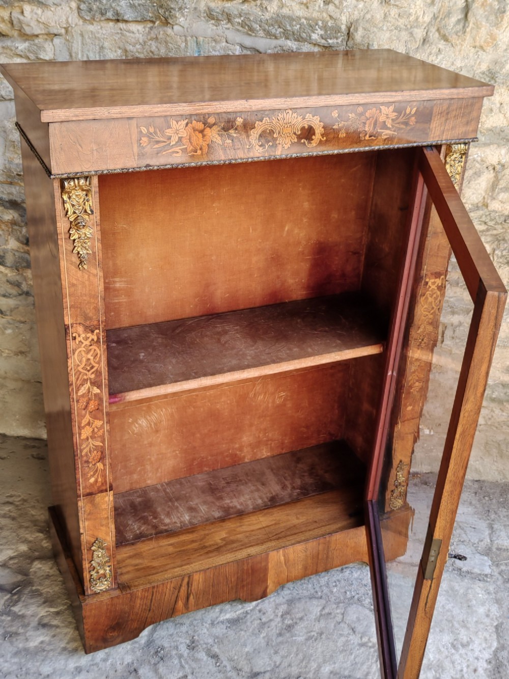 A Victorian walnut pier cabinet featuring floral marquetry inlay, gilt-bronze mounts, and a single glazed glass door opening to two interior shelves. View VI