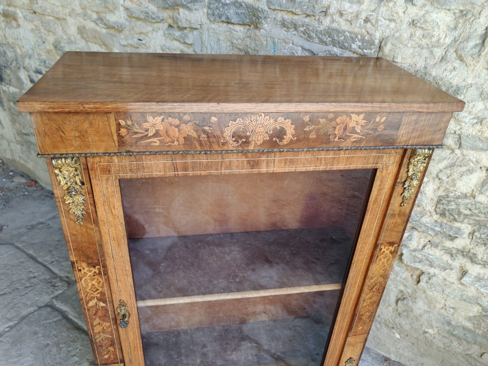 A Victorian walnut pier cabinet featuring floral marquetry inlay, gilt-bronze mounts, and a single glazed glass door opening to two interior shelves. View VIII