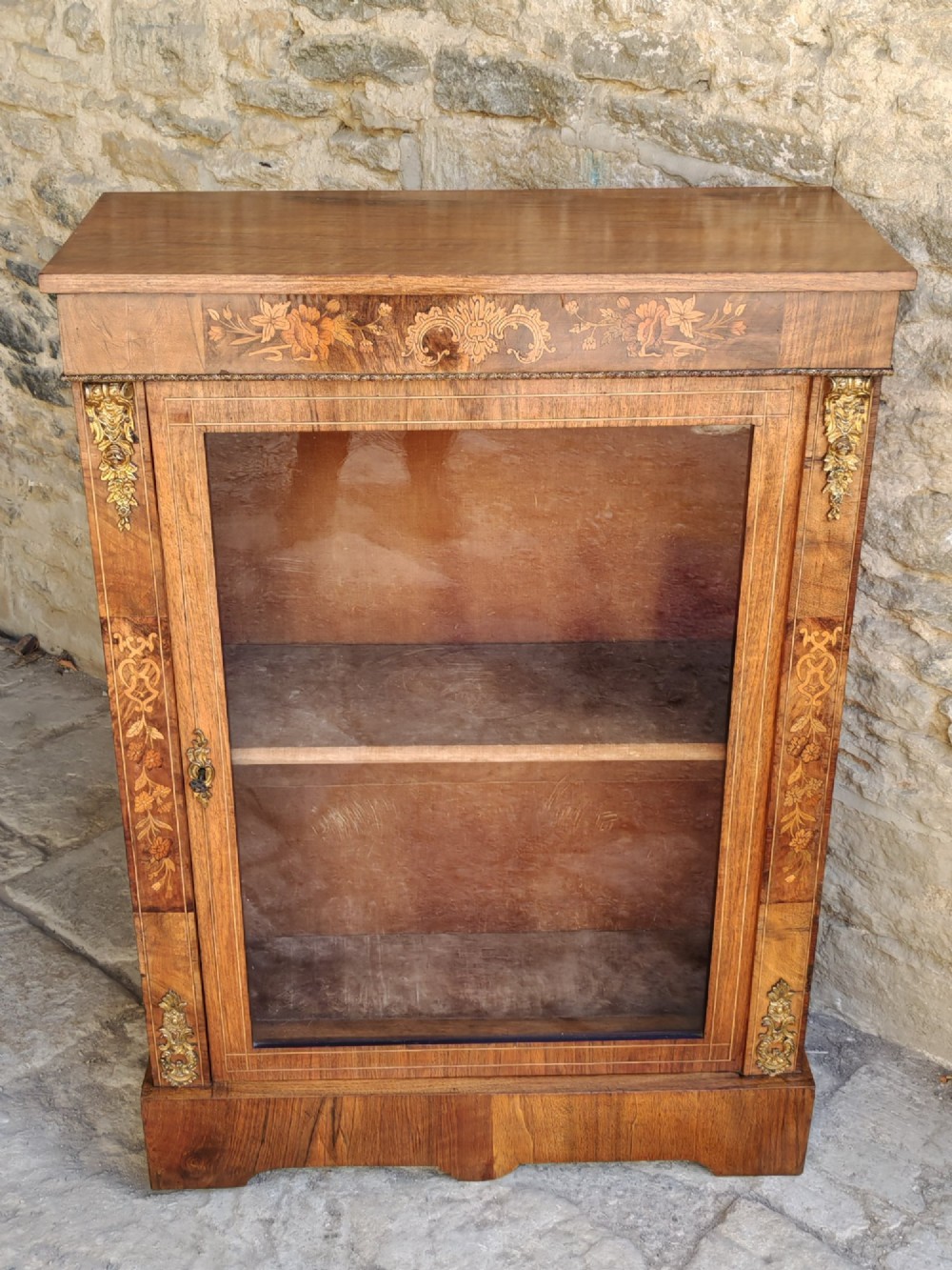 A Victorian walnut pier cabinet featuring floral marquetry inlay, gilt-bronze mounts, and a single glazed glass door opening to two interior shelves. View IX