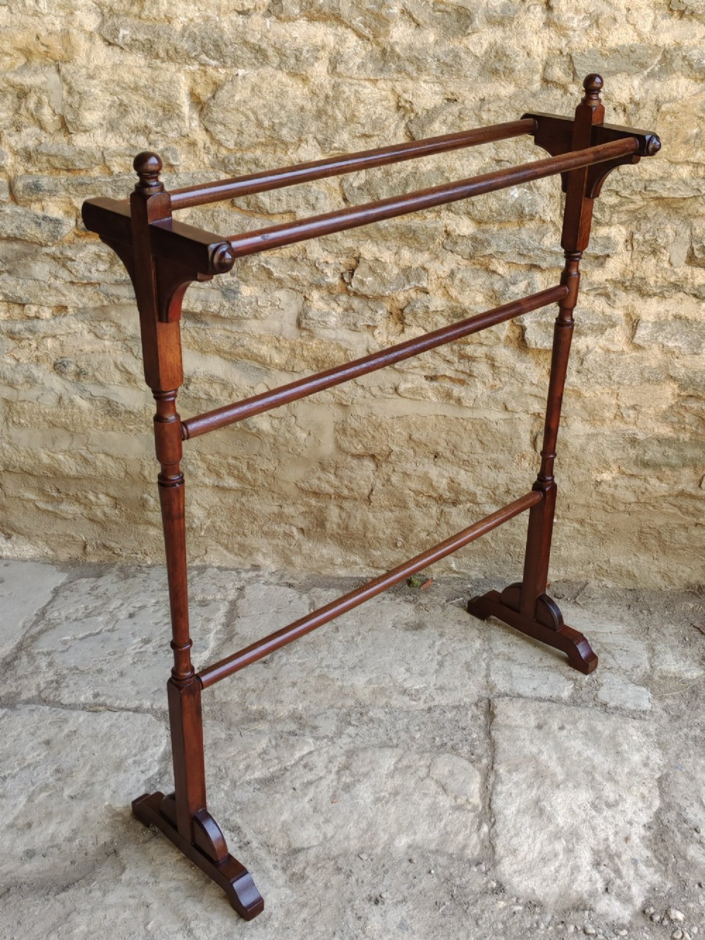 A Victorian dark mahogany freestanding towel rail featuring turned uprights with top finials, multiple horizontal bars, and carved trestle feet.