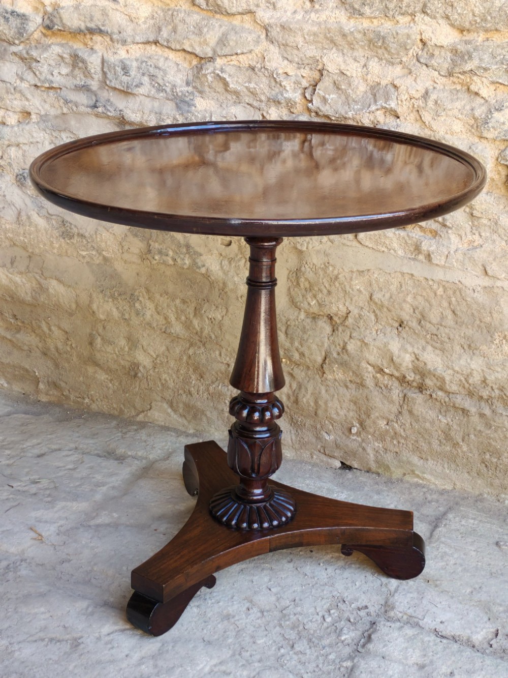 A circular Regency dishtop occasional table made of dark wood with a turned pedestal stem and triform base. View VII