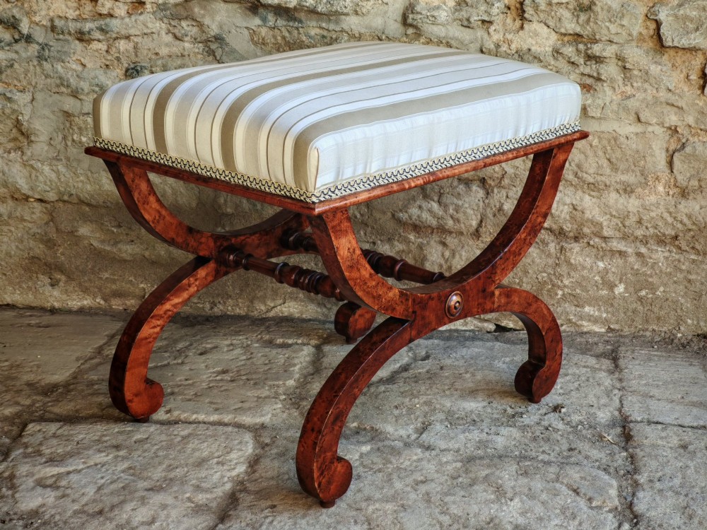 A mid-19th-century x-frame stool featuring burr maple wood curves, a turned central stretcher, scroll feet, and a beige and white striped upholstered seat. View VI