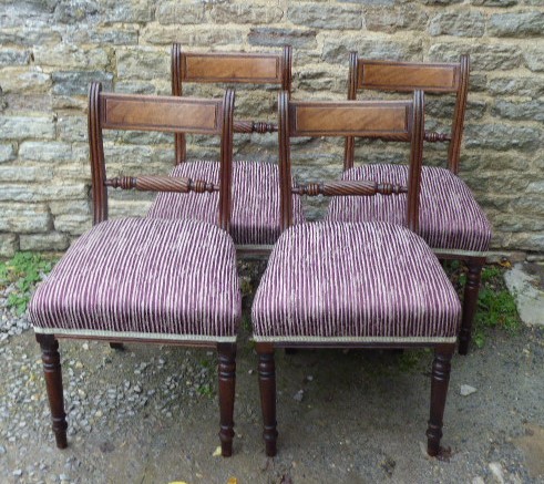 A set of four Regency mahogany dining chairs featuring carved rope-twist cross rails, reeded uprights, turned front legs, and plum striped upholstered seats.