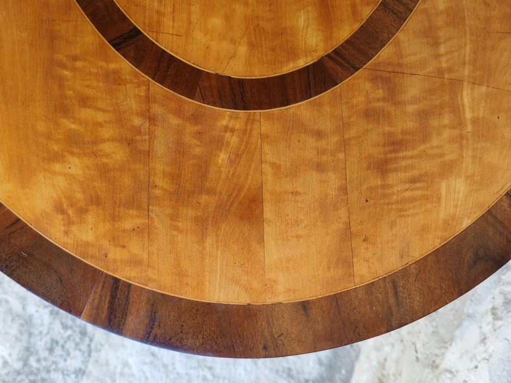 An oval satinwood coffee table featuring double band inlay on the tabletop and supported by twin trestle legs connected by a central stretcher. View III