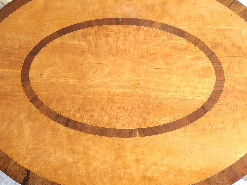 An oval satinwood coffee table featuring double band inlay on the tabletop and supported by twin trestle legs connected by a central stretcher. View IV