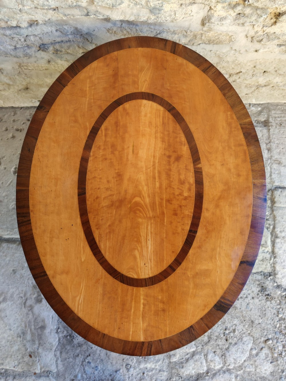 An oval satinwood coffee table featuring double band inlay on the tabletop and supported by twin trestle legs connected by a central stretcher. View VIII