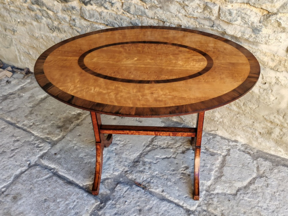 An oval satinwood coffee table featuring double band inlay on the tabletop and supported by twin trestle legs connected by a central stretcher. View IX