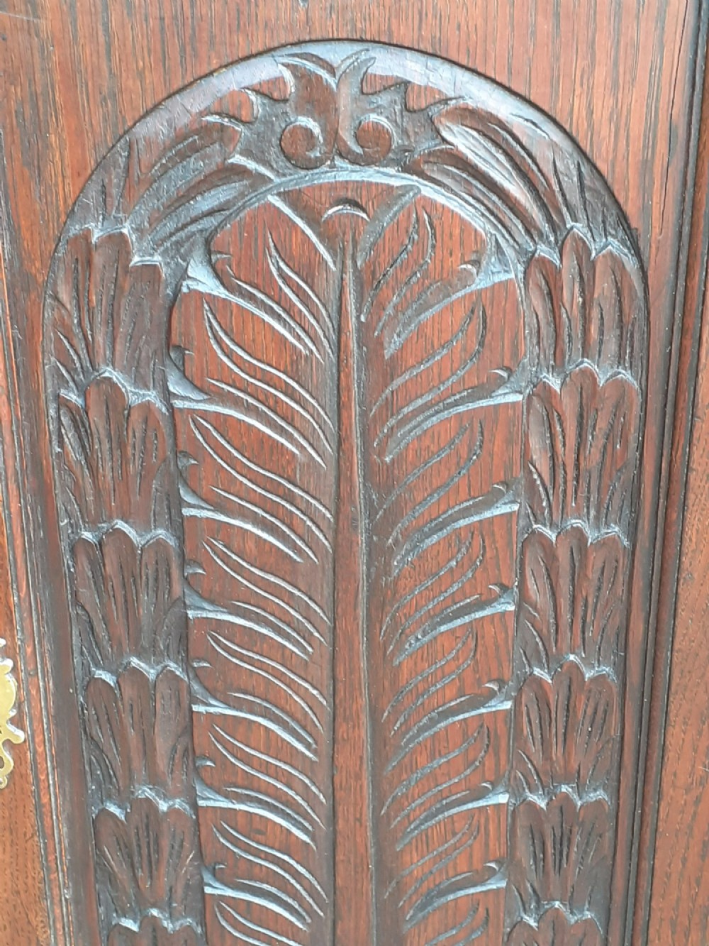 An 18th-century dark oak hanging corner cupboard featuring a hand-carved foliate panel on its single door and a brass keyhole escutcheon. View III