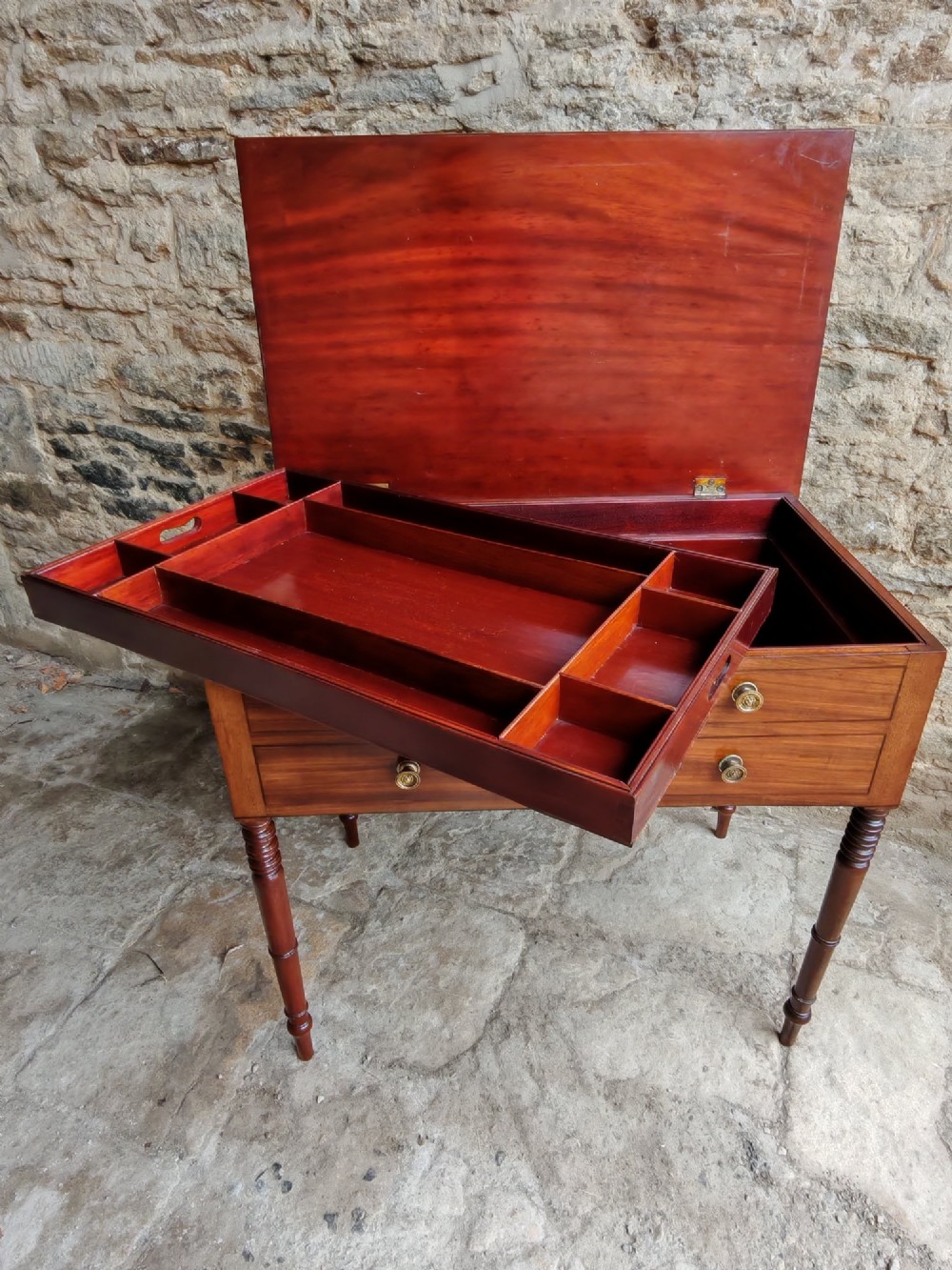 A mid-19th century mahogany work table with an open hinged lid revealing a removable fitted compartment tray set atop turned legs.