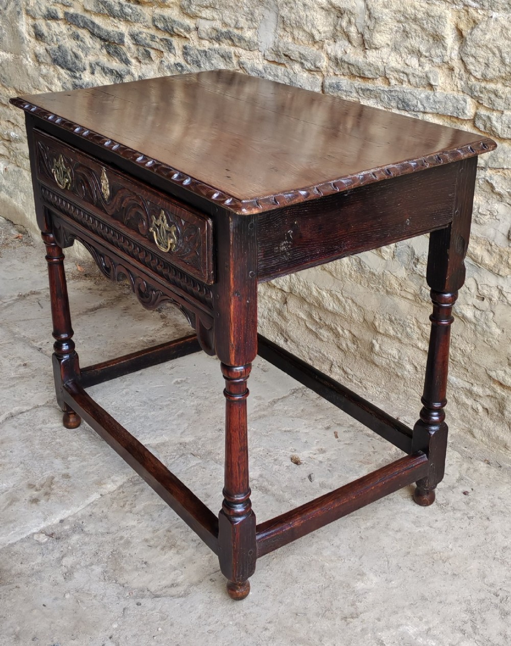 An 18th-century dark oak lowboy featuring a single relief-carved drawer with brass handles, turned front legs, and a shaped carved apron. View VII