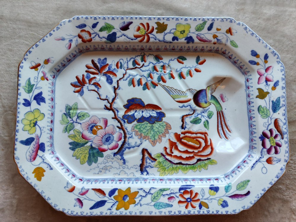An octagonal Masons ironstone meat platter decorated with a multi-coloured hand-painted chinoiserie motif featuring a bird, flowering branches, and integrated drainage grooves.