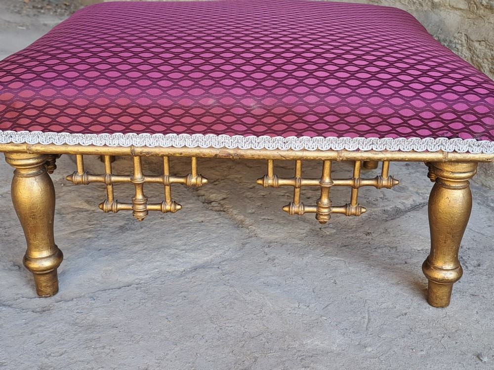 A low rectangular footstool featuring a patterned burgundy padded top with silver braid trim and a gilded wood frame with turned legs and lattice fretwork details. View II