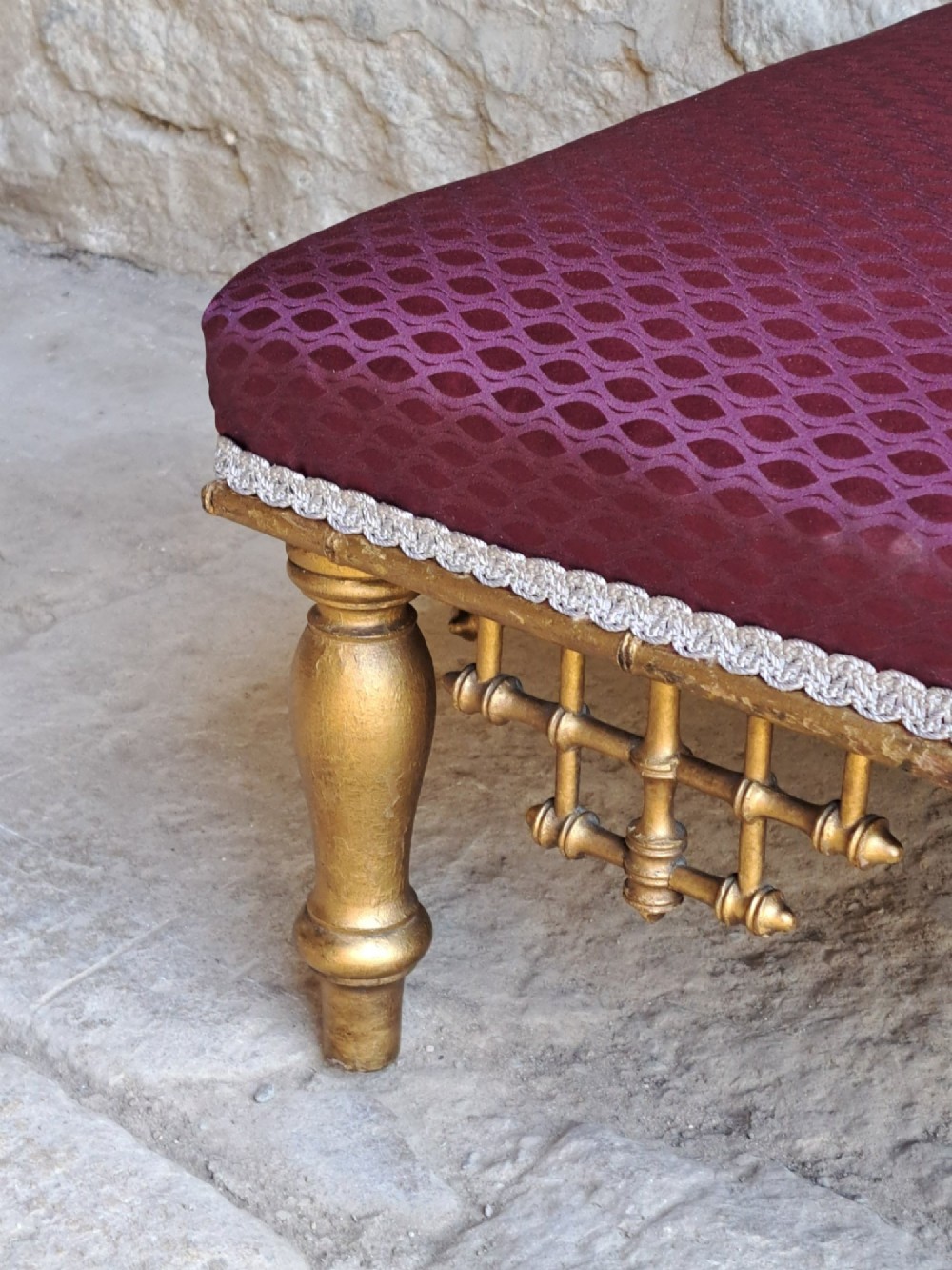 A low rectangular footstool featuring a patterned burgundy padded top with silver braid trim and a gilded wood frame with turned legs and lattice fretwork details. View IV
