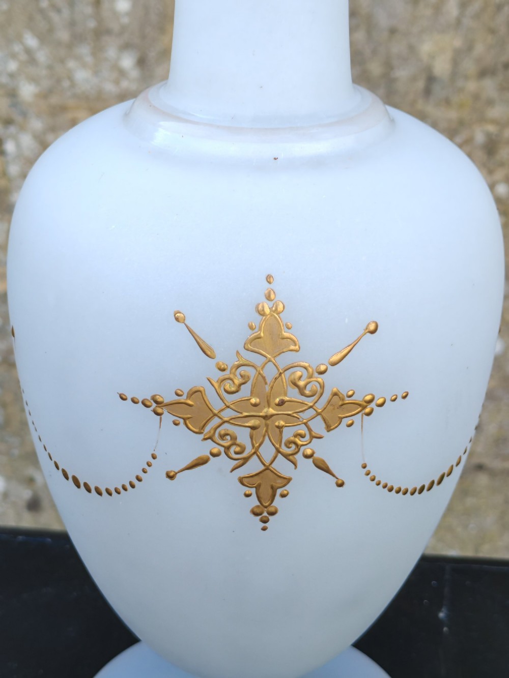 A white opaline glass vase featuring a slender neck, a pedestal base, gold filigree detailing, and a black classical profile cameo medallion at the centre. View VI