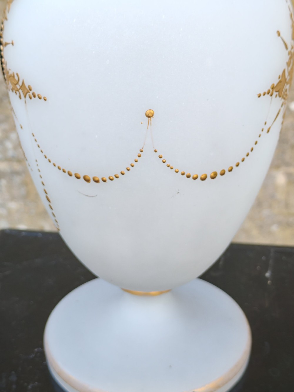 A white opaline glass vase featuring a slender neck, a pedestal base, gold filigree detailing, and a black classical profile cameo medallion at the centre. View VII