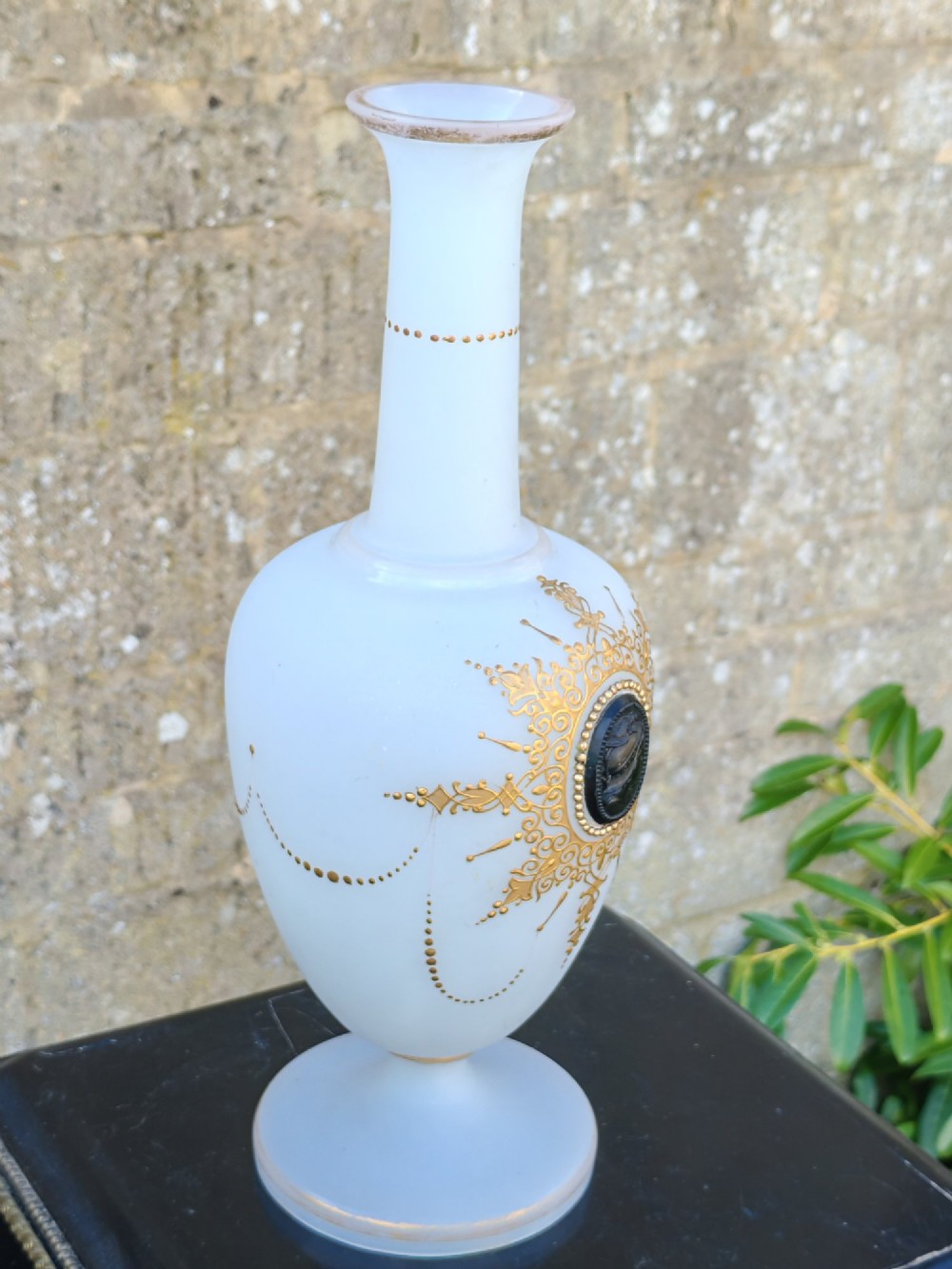 A white opaline glass vase featuring a slender neck, a pedestal base, gold filigree detailing, and a black classical profile cameo medallion at the centre. View VIII