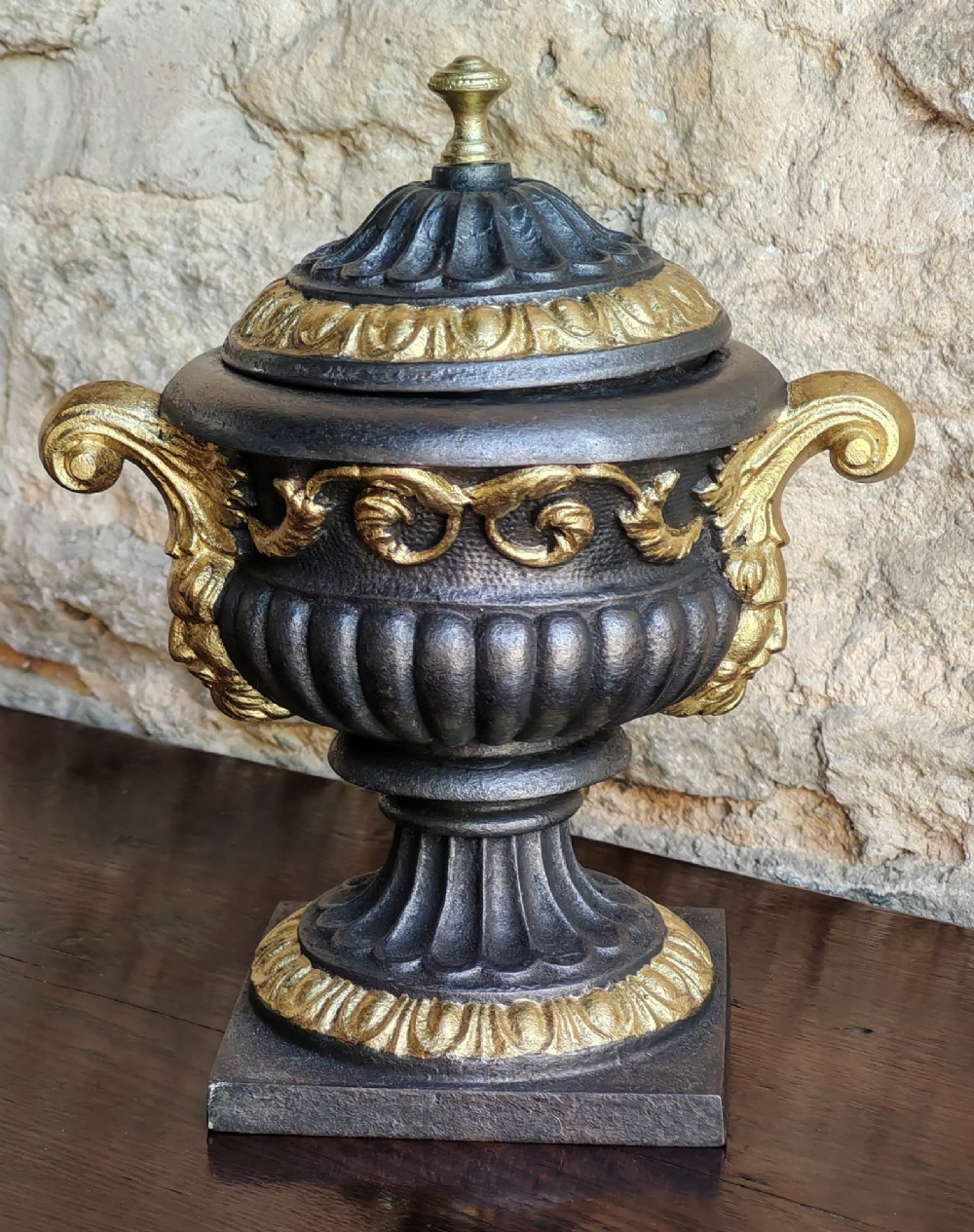 A Victorian cast iron covered urn with parcel-gilded acanthus handles, a gadrooned lid, and a square base.