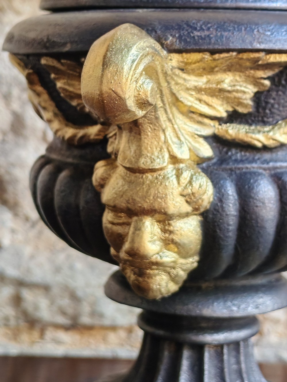 A Victorian cast iron covered urn with parcel-gilded acanthus handles, a gadrooned lid, and a square base. View II
