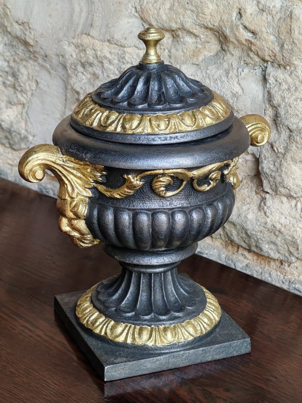 A Victorian cast iron covered urn with parcel-gilded acanthus handles, a gadrooned lid, and a square base. View IV