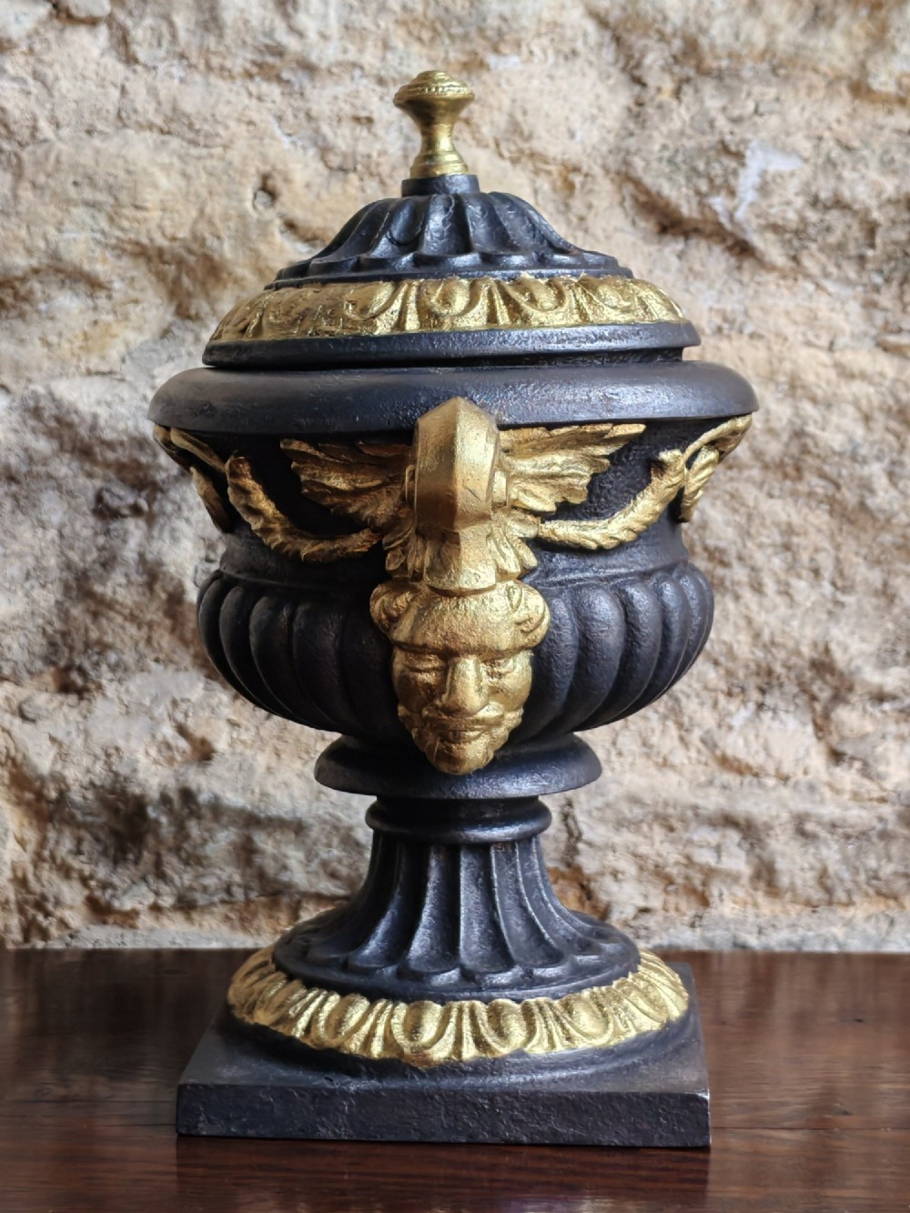 A Victorian cast iron covered urn with parcel-gilded acanthus handles, a gadrooned lid, and a square base. View V