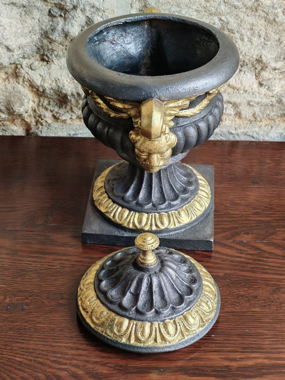 A Victorian cast iron covered urn with parcel-gilded acanthus handles, a gadrooned lid, and a square base. View VI