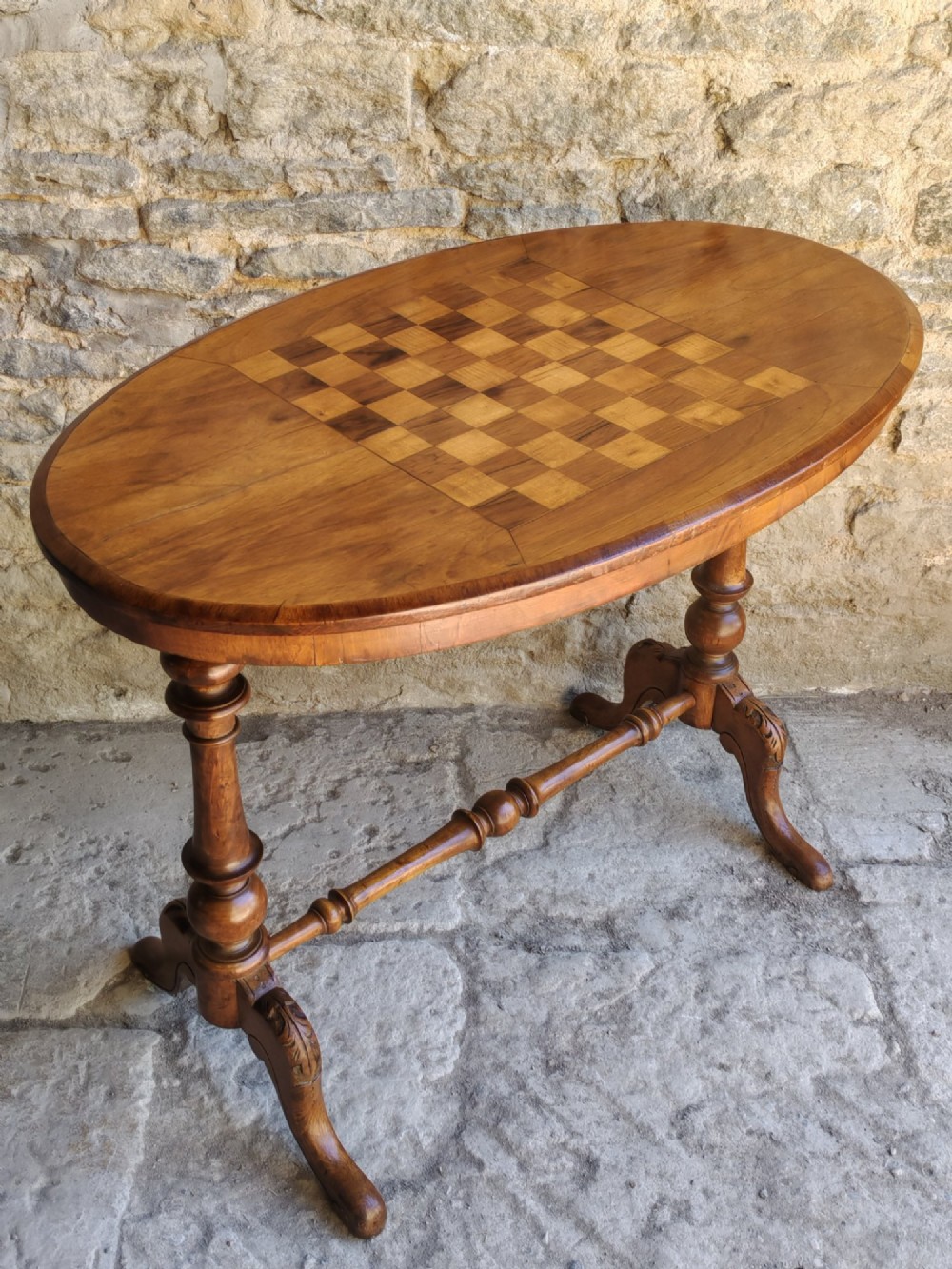 A late 19th-century oval walnut games table featuring an inlaid chessboard top, turned end supports, a central stretcher, and carved legs.