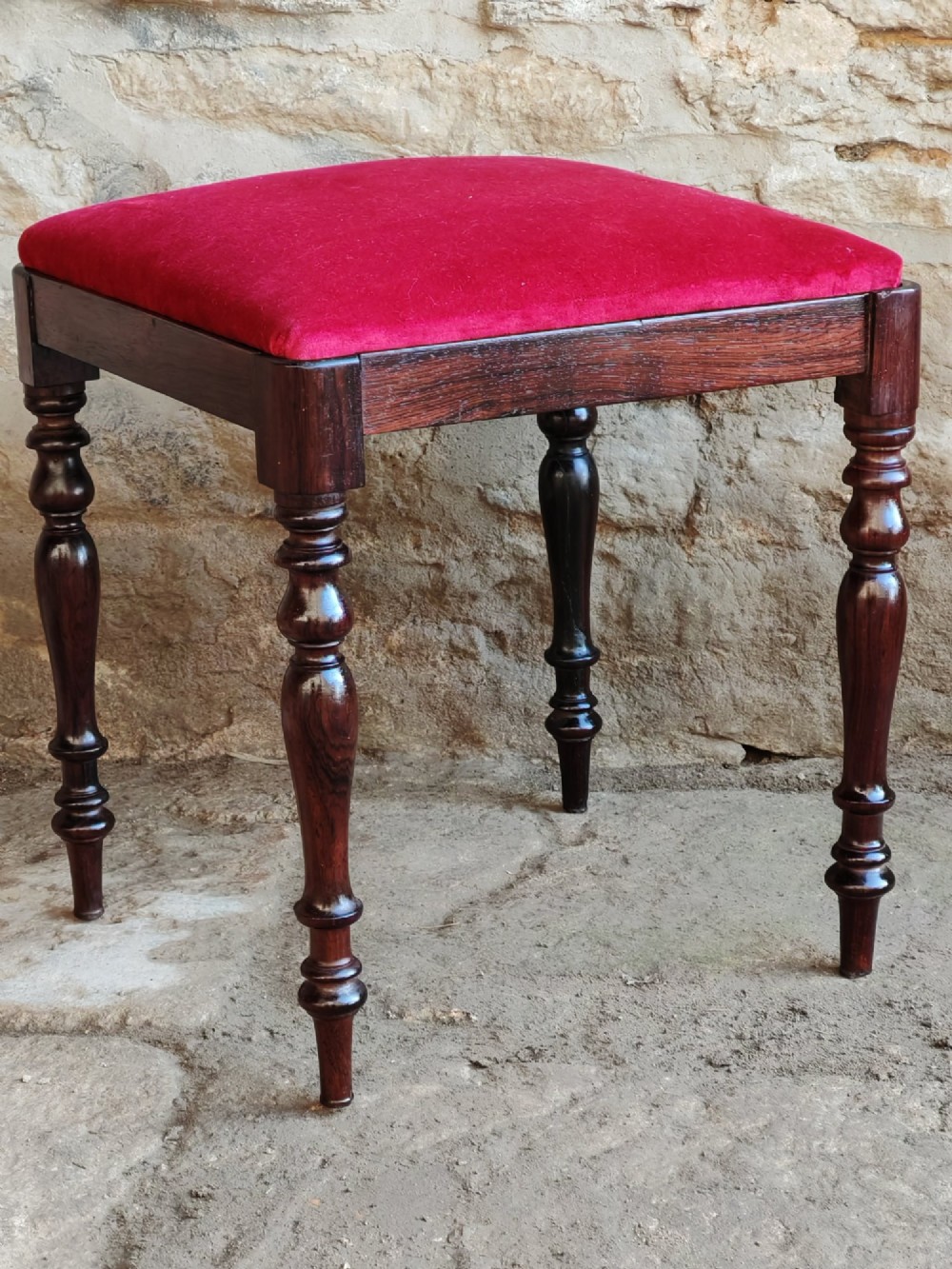 An antique square rosewood stool featuring turned legs and a red velvet upholstered seat.