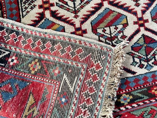 fig 1. An antique Caucasian Shirvan hand-knotted wool rug featuring a central cream field with geometric diamond lattice motifs framed by multiple red and blue patterned borders.