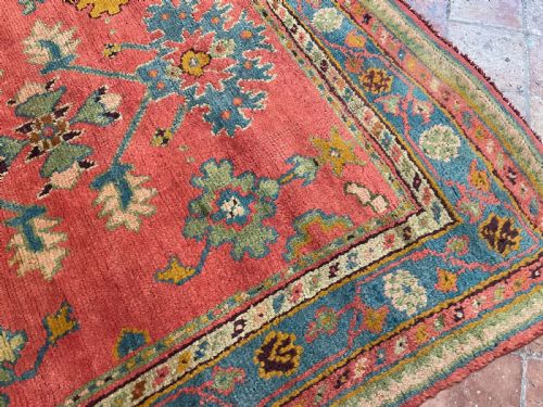 fig 1. A square antique Turkish Ushak hand-knotted wool rug featuring a crimson field with teal floral medallions and a broad patterned blue border.