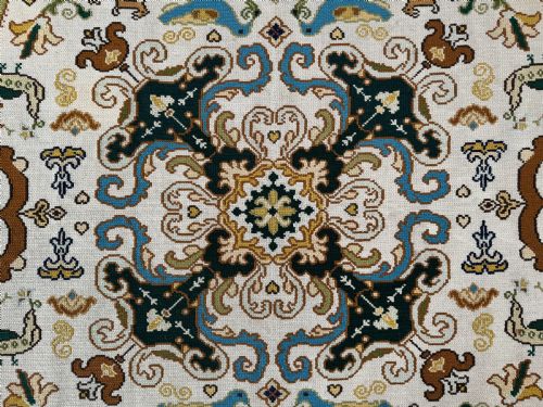 fig 1. A rectangular handstitched Portuguese needlepoint rug featuring a cream central field with scrolling foliage, bird motifs, and a dark ornate border.