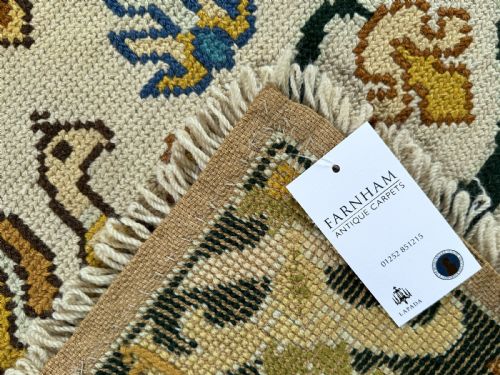fig 3. A rectangular handstitched Portuguese needlepoint rug featuring a cream central field with scrolling foliage, bird motifs, and a dark ornate border.
