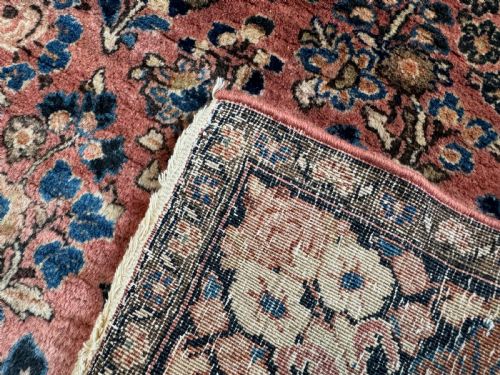 fig 2. A rectangular hand-knotted antique Sarouk rug featuring intricate floral sprays in blue and cream across a terracotta red field with a dark blue multi-banded border.