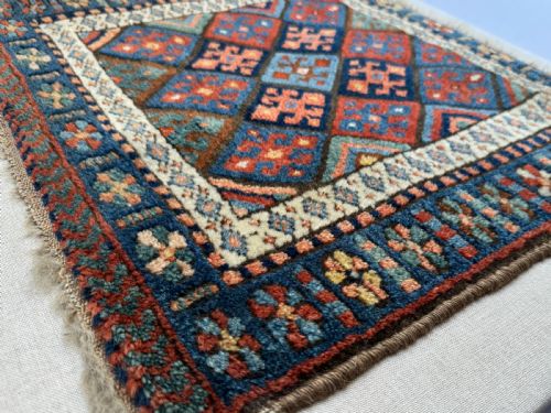 fig 2. A square antique woven wool Jaf Kurdish bag face featuring geometric diamond lattice patterns in blue, red, ochre, and cream colours.