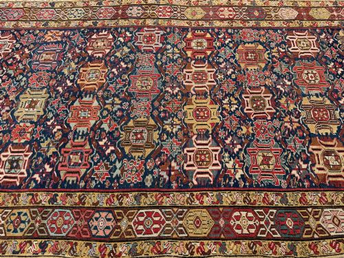 fig 1. An elongated antique hand-knotted Caucasian Kuba Kelleh rug with a navy blue field featuring geometric repeating medallions framed by patterned multicoloured borders.