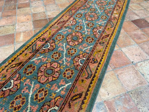 fig 2. An exceptionally long antique Ushak runner rug displaying a central slate blue panel with repeating coral floral rosettes framed by a wide terracotta patterned border.
