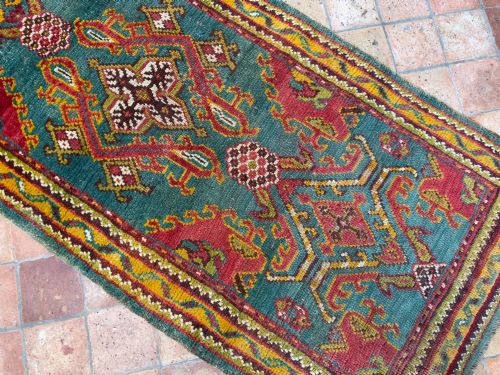 fig 1. An antique hand-knotted wool runner rug featuring geometric tribal medallions in red, yellow, and orange on a vibrant teal background.