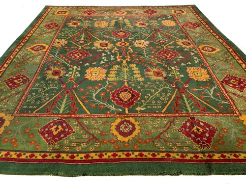fig 2. An antique Arts and Crafts hand-knotted wool Donegal carpet featuring a green field filled with stylised red and yellow floral motifs and a decorative geometric border.
