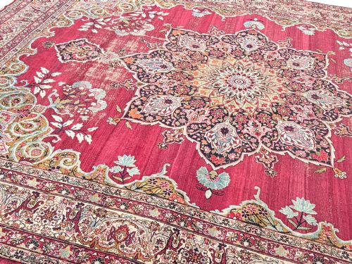 fig 1. An antique hand-knotted Kirman wool carpet featuring a large central starburst medallion surrounded by floral borders on a crimson red field with distressed wear.