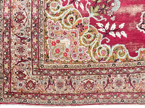 fig 2. An antique hand-knotted Kirman wool carpet featuring a large central starburst medallion surrounded by floral borders on a crimson red field with distressed wear.