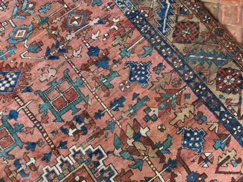 fig 3. An antique Persian Heriz hand-knotted carpet featuring a terracotta red field filled with geometric motifs, enclosed by a blue and beige patterned border.
